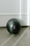 Black pilates ball with barre belle logo on a gray floor against a white wall