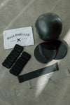Black pilates ball and accessories on a concrete floor with 'Belle Babe Club' branding. Tonal resistance bands and sliders and ankle weights.
