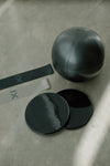 black pilates ball, black sliders, and black and light grey resistance band pilates barre equipment set on grey background