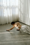 Person in a white outfit using sliders on marble floor for barre pilates workout with sheer curtains in the background