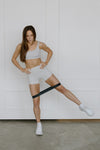 Woman exercising with black heavy resistance band against a white wall.