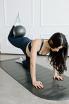 Pregnant woman exercising in a barre pilates pose on a mat with a pilates ball in the background