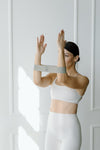 Woman in white athletic wear practicing barre and pilates witha. tonal resistance band in a bright room with white walls.